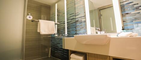 A modern bathroom with a glass-enclosed shower, a large mirror, and a vanity with a sink and towel storage.