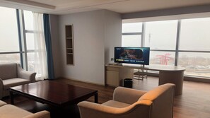 Ein modernes Hotelzimmer mit großem Fenster, Flachbildfernseher, Holztisch und zwei Sesseln.