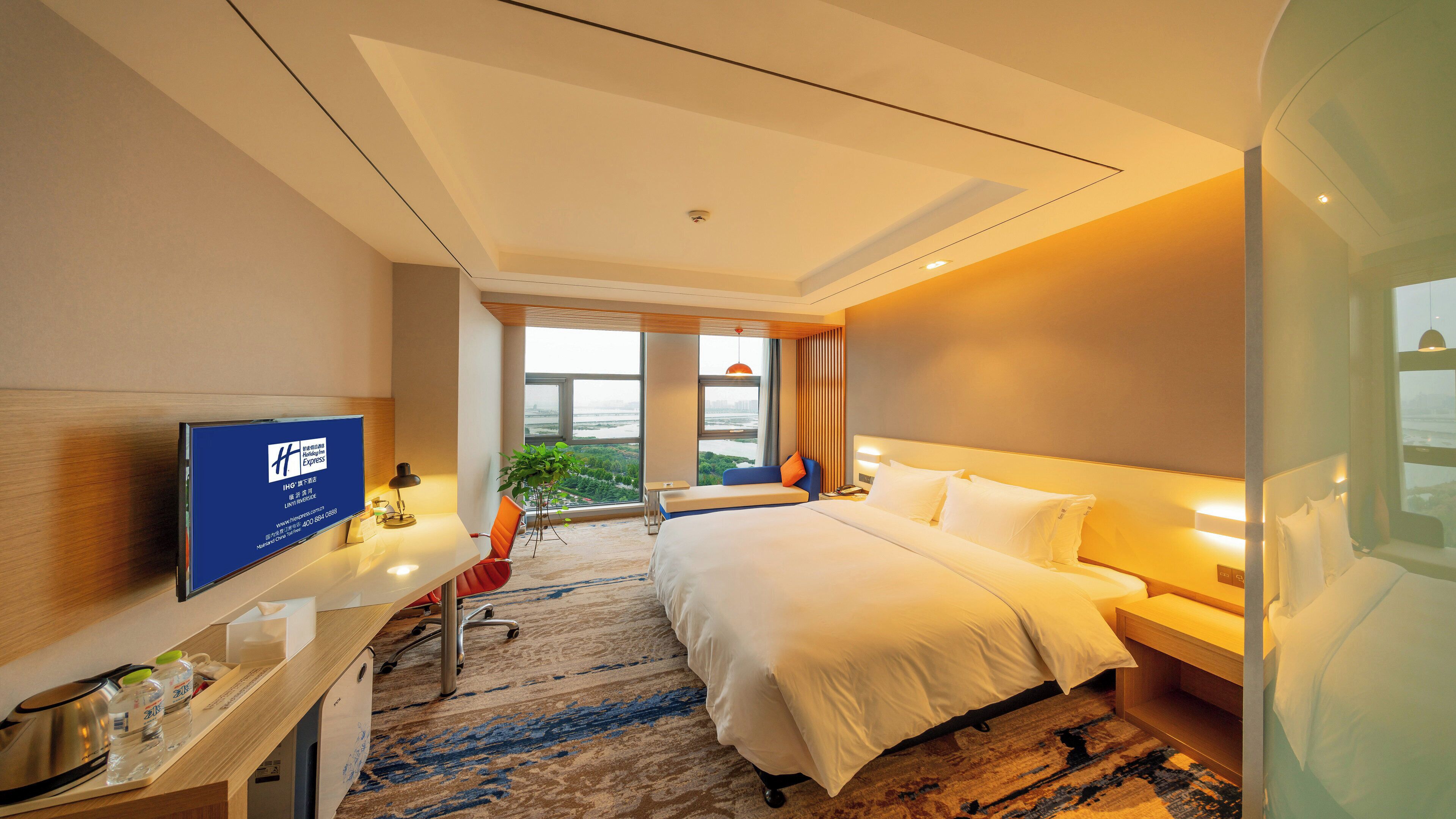 Habitación de hotel con una cama, un escritorio con ordenador, televisor y un amplio ventanal con vistas.