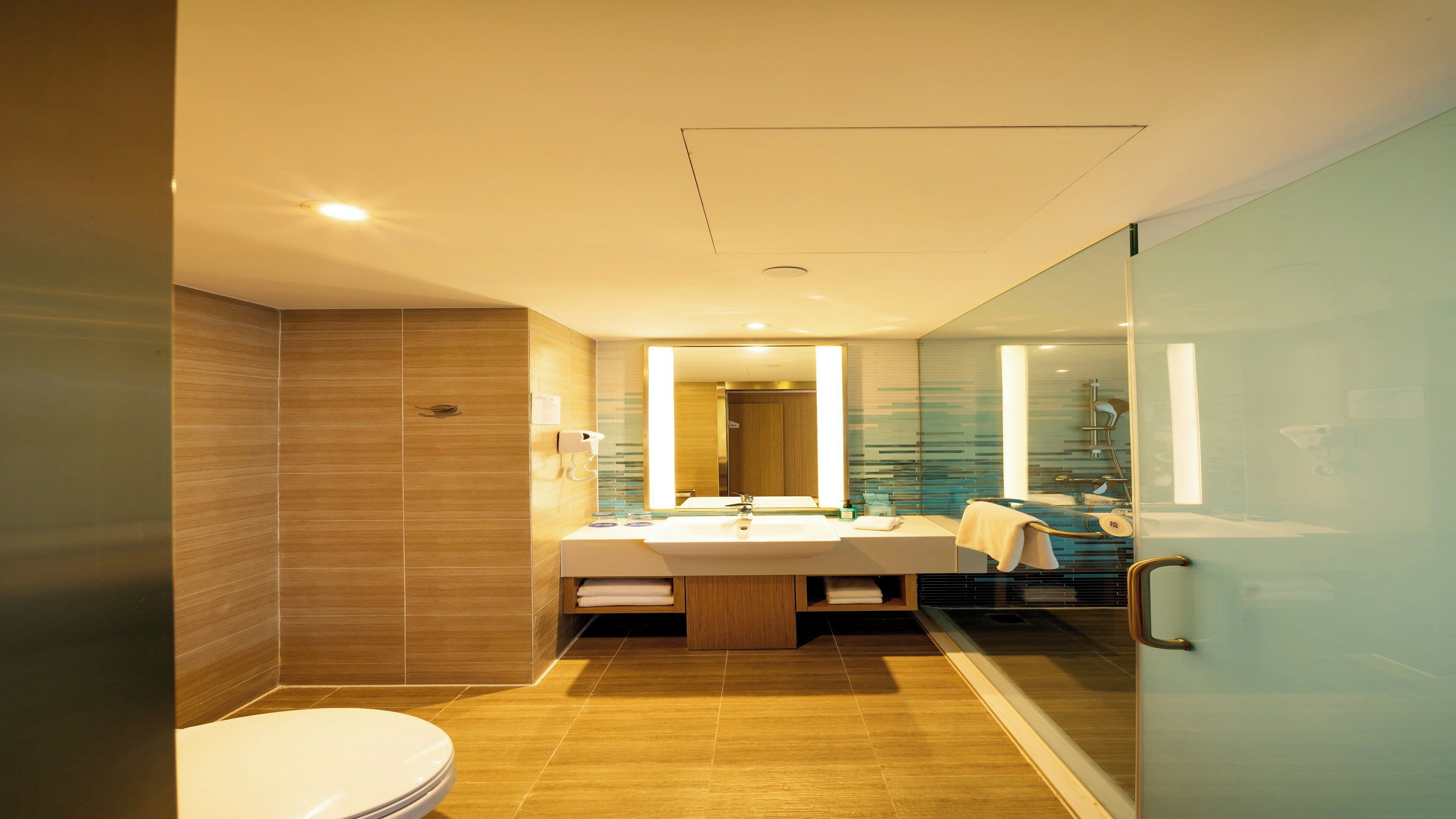A modern bathroom with a glass shower enclosure, a large mirror, and a wooden vanity.