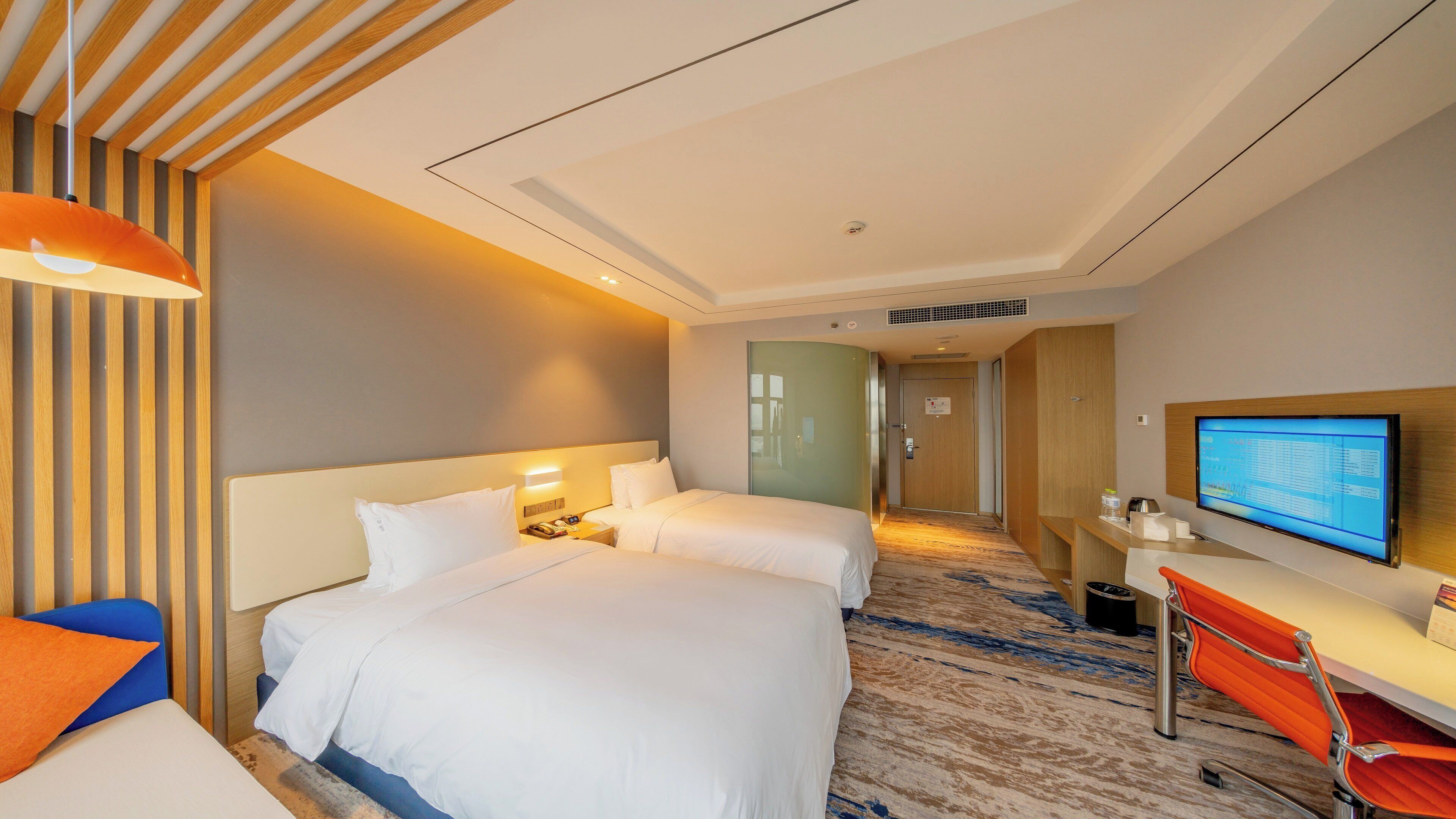 A hotel room with a bed, bedside tables, a desk with a computer, and a television.