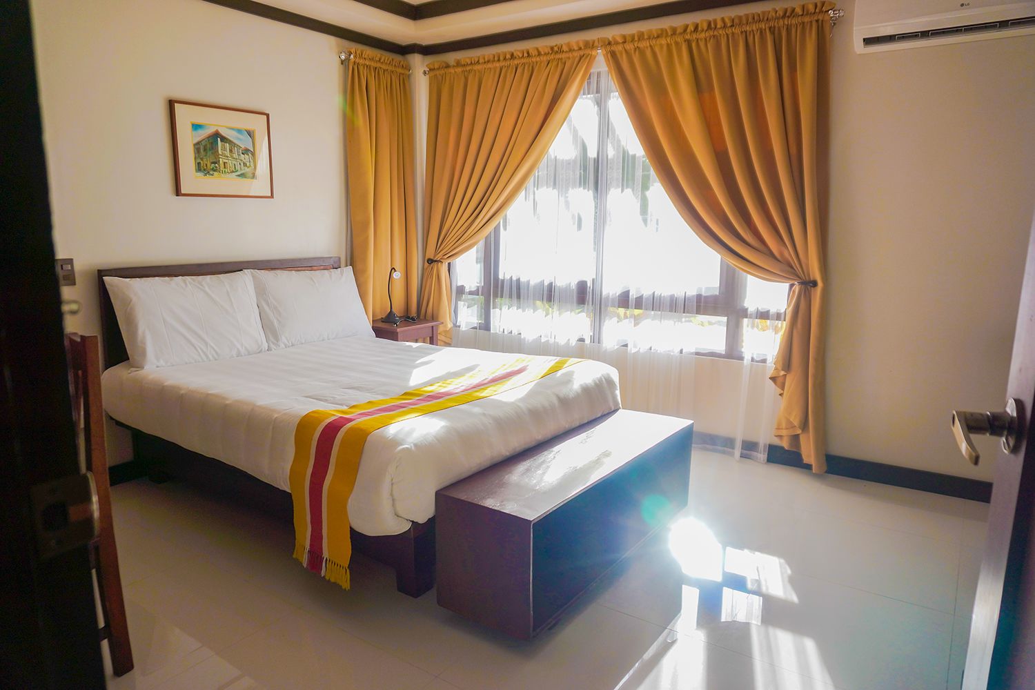 A hotel room with a bed, a bedside table, a lamp, and a window with curtains.