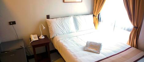 Habitación de hotel con cama, mesita de noche con teléfono y lámpara, escritorio pequeño y ventana con cortinas.