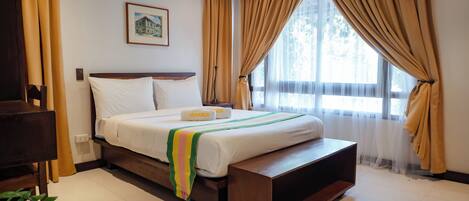 A neatly made bed with a white comforter and pillows, a wooden bench at the foot of the bed, and a framed picture on the wall.