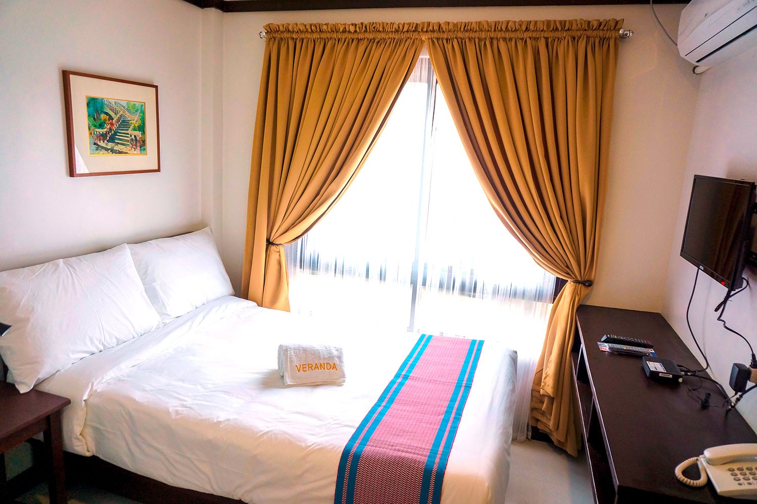 A hotel room with a bed, a desk with a telephone, and a television.