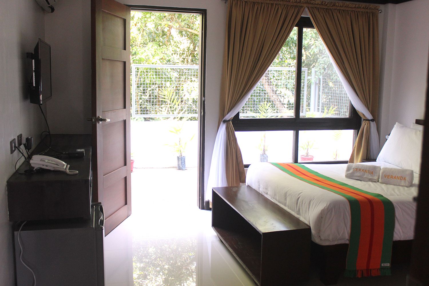 A hotel room with a bed, a desk with a telephone, and a window with curtains.