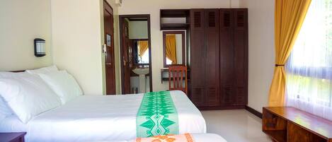 A hotel room with two beds, a wooden wardrobe, a bench, and a bathroom visible through an open door.