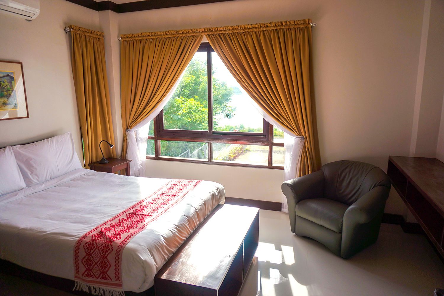 A hotel room with a bed, a chair, a desk, and a window with curtains.
