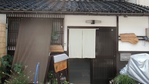 Ein traditionelles japanisches Haus mit Ziegeldach, hölzernem Eingangstor und einem kleinen Garten mit Topfpflanzen.