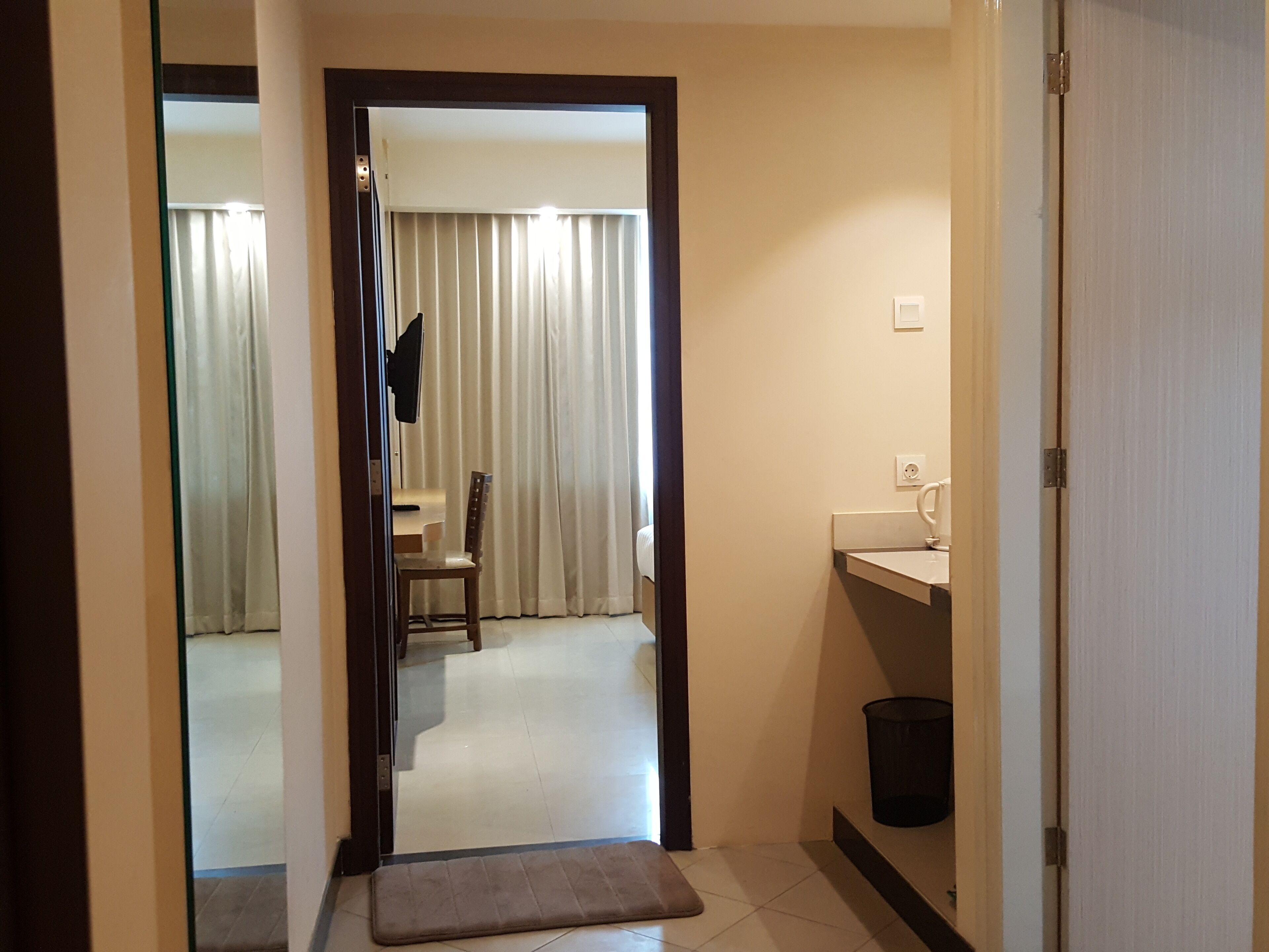 A hotel hallway with a wooden door, a bench, a chair, a sink, and a trash can.