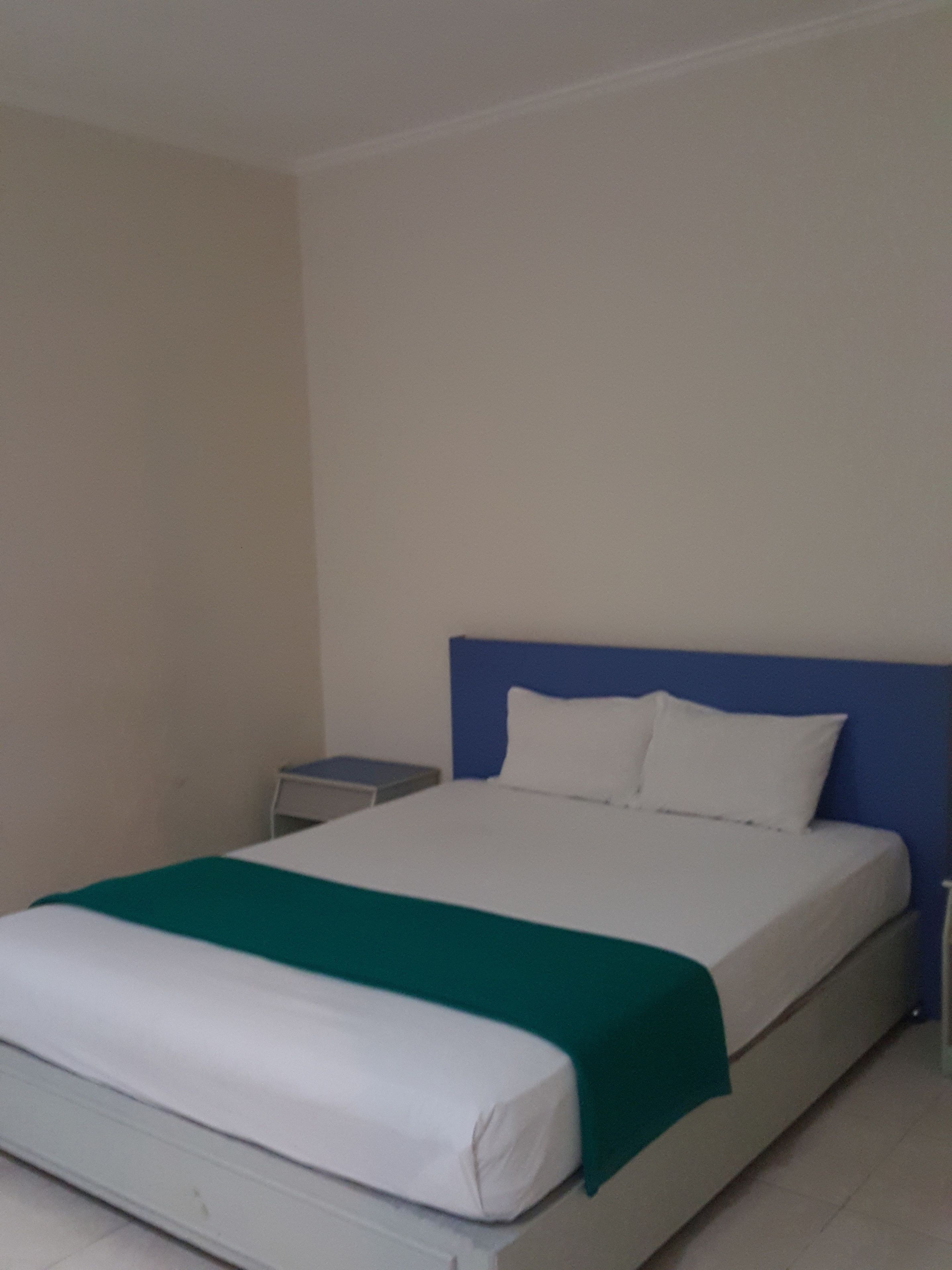 A single-bed room with a white mattress, a green blanket, and a blue headboard.