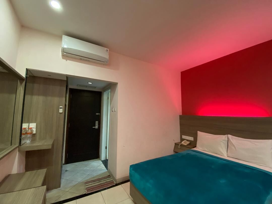 A hotel room with a bed, a nightstand, a desk, and an air conditioning unit.