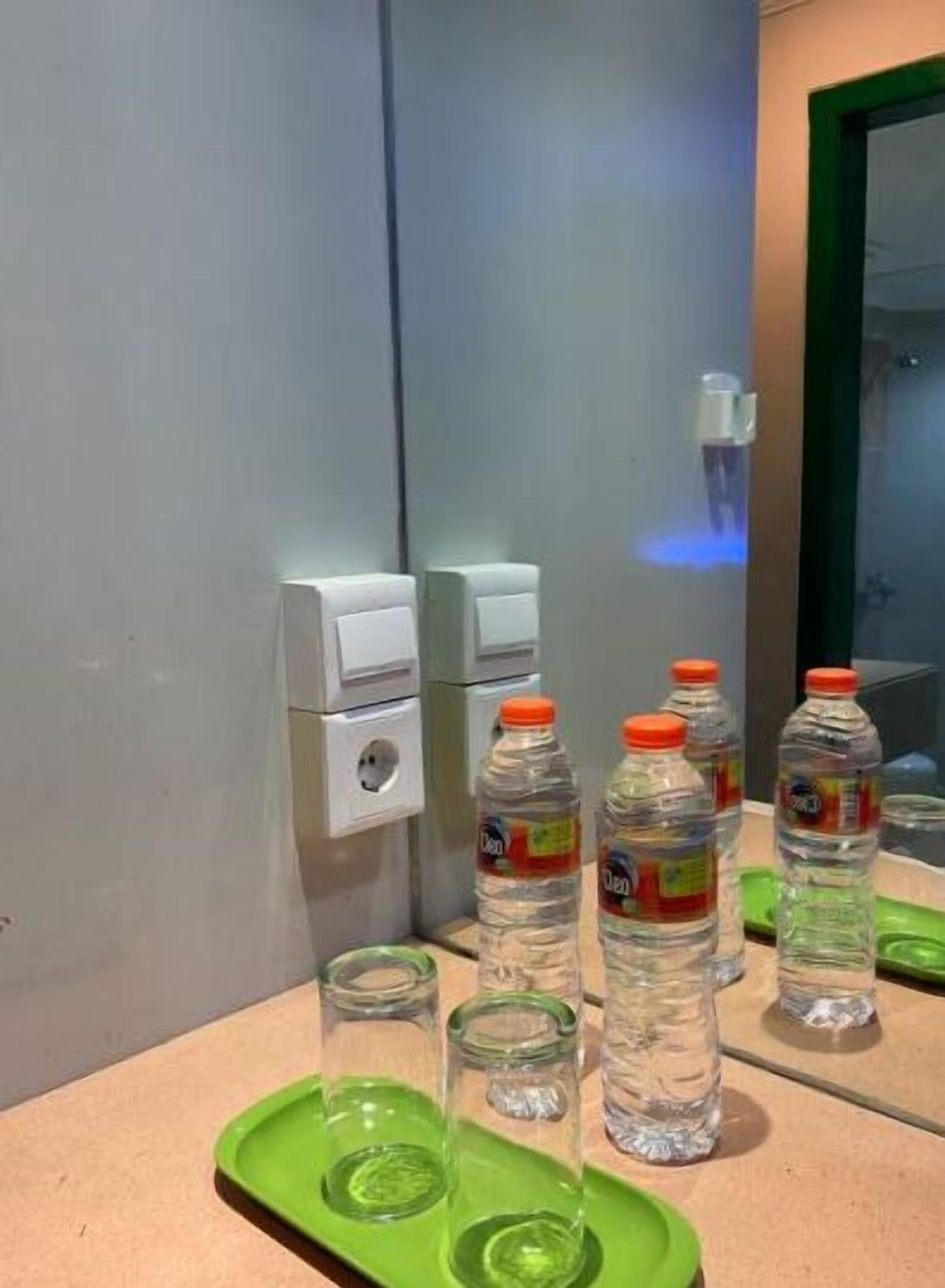 A restroom with a mirror, a hand dryer, and several water bottles and glasses on a counter.
