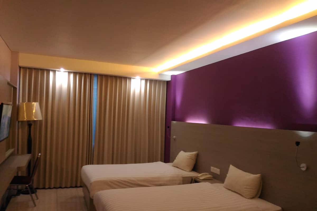 A hotel room with two beds, a desk, a lamp, and a TV.