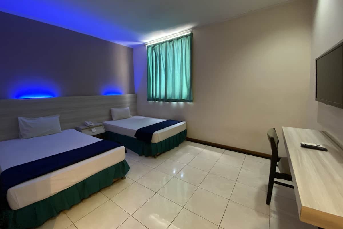 A hotel room with two beds, a desk, a TV, and a window with curtains.