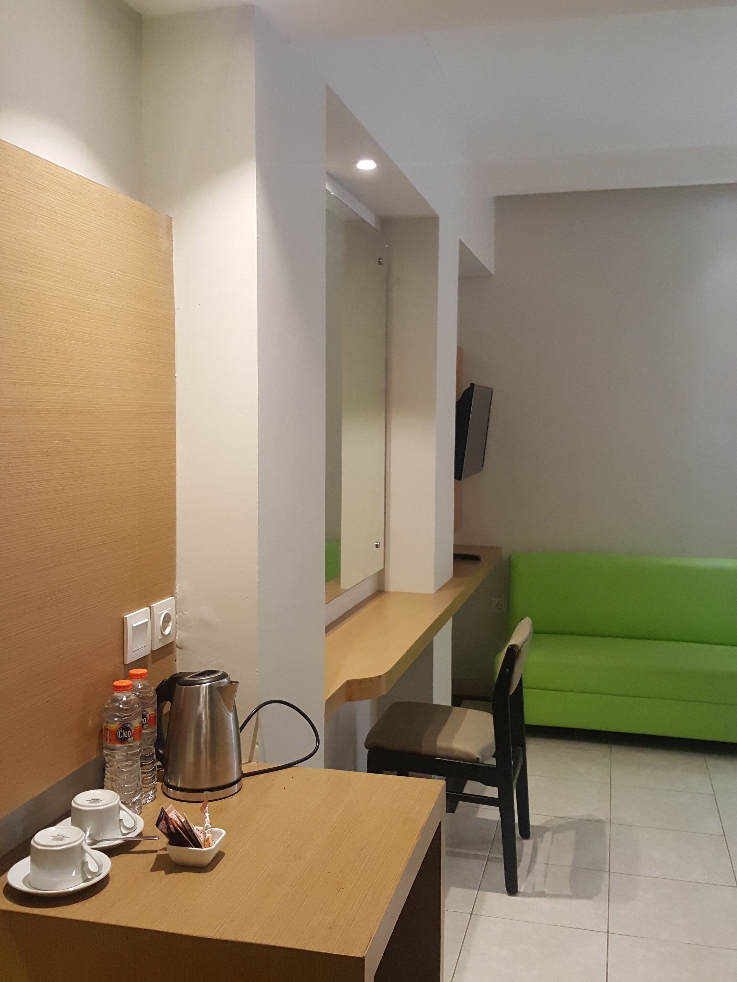 Habitació d'hotel moderna amb un escriptori de fusta, un sofà verd, una televisió i un mirall.