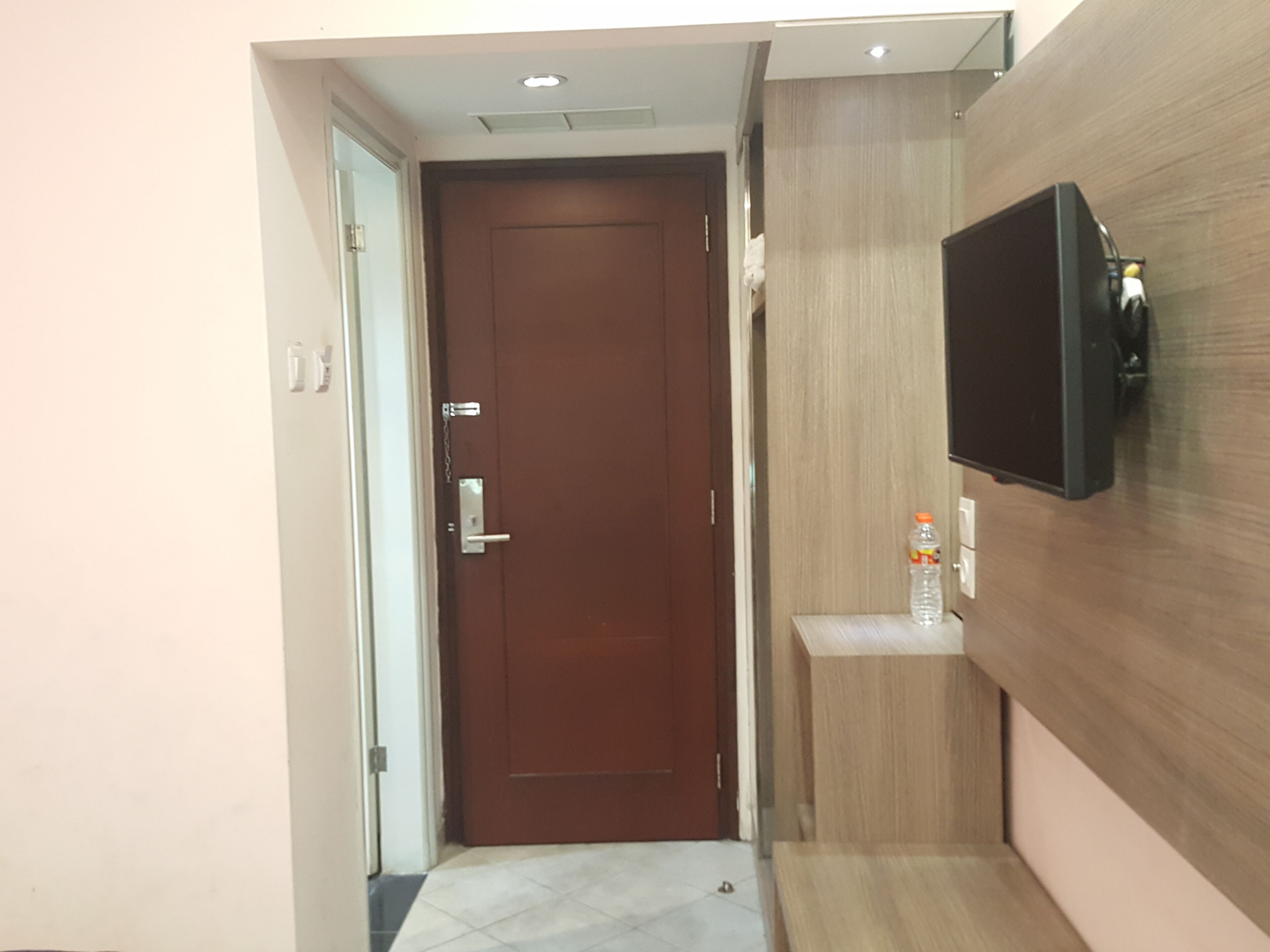 A hallway with a wooden door, a mounted television, and a small shelf with a bottle.