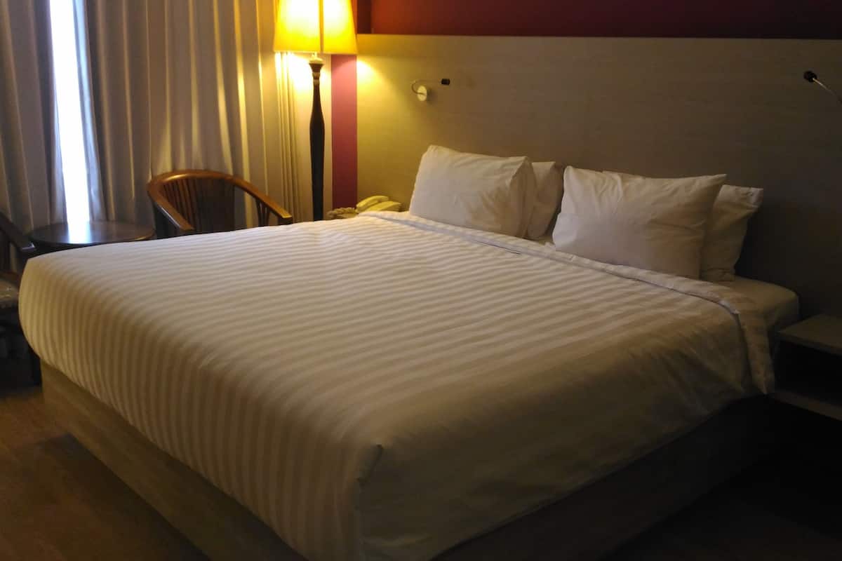 A hotel room with a large bed, a nightstand, a lamp, and a chair.
