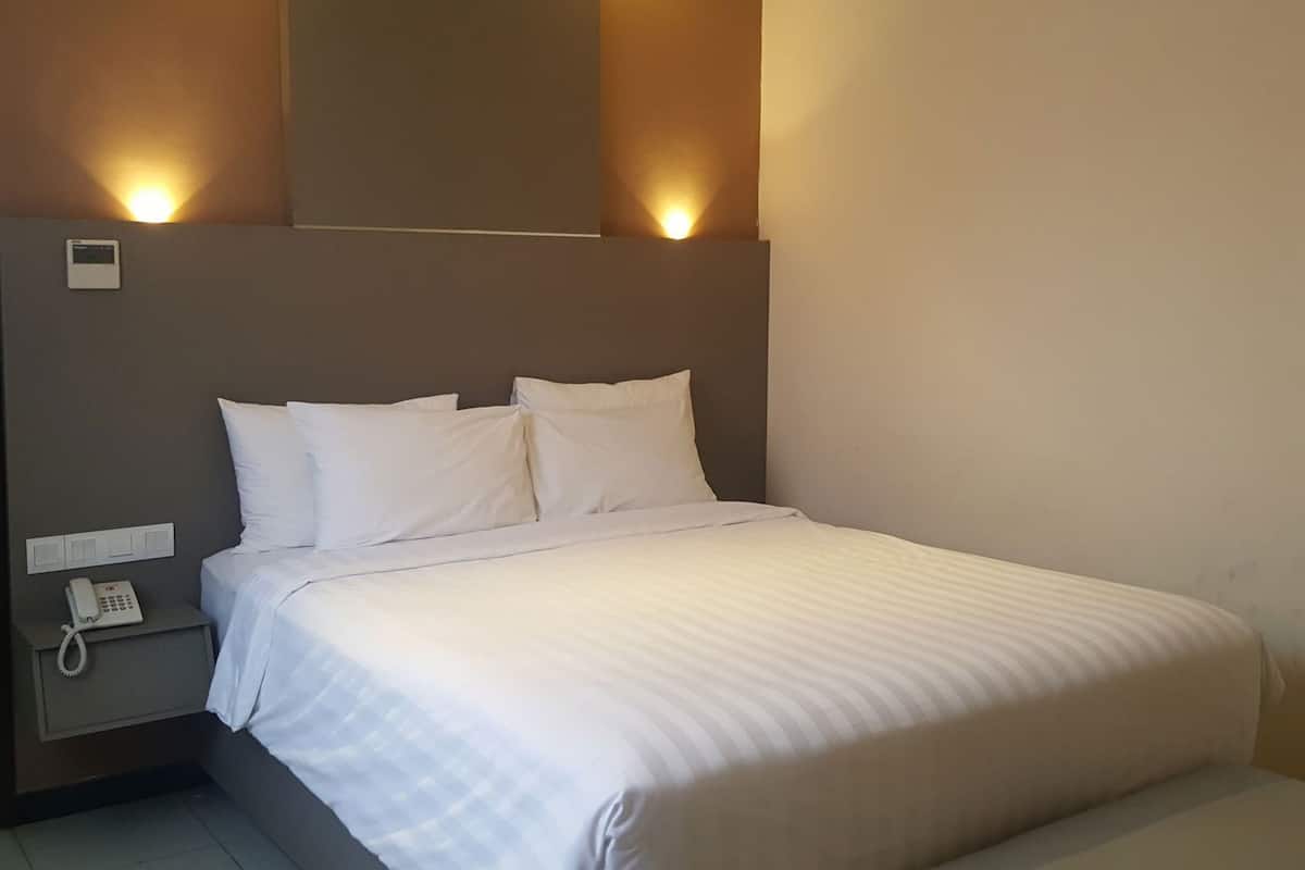 A hotel room with a bed, a bedside telephone, and wall-mounted lighting.