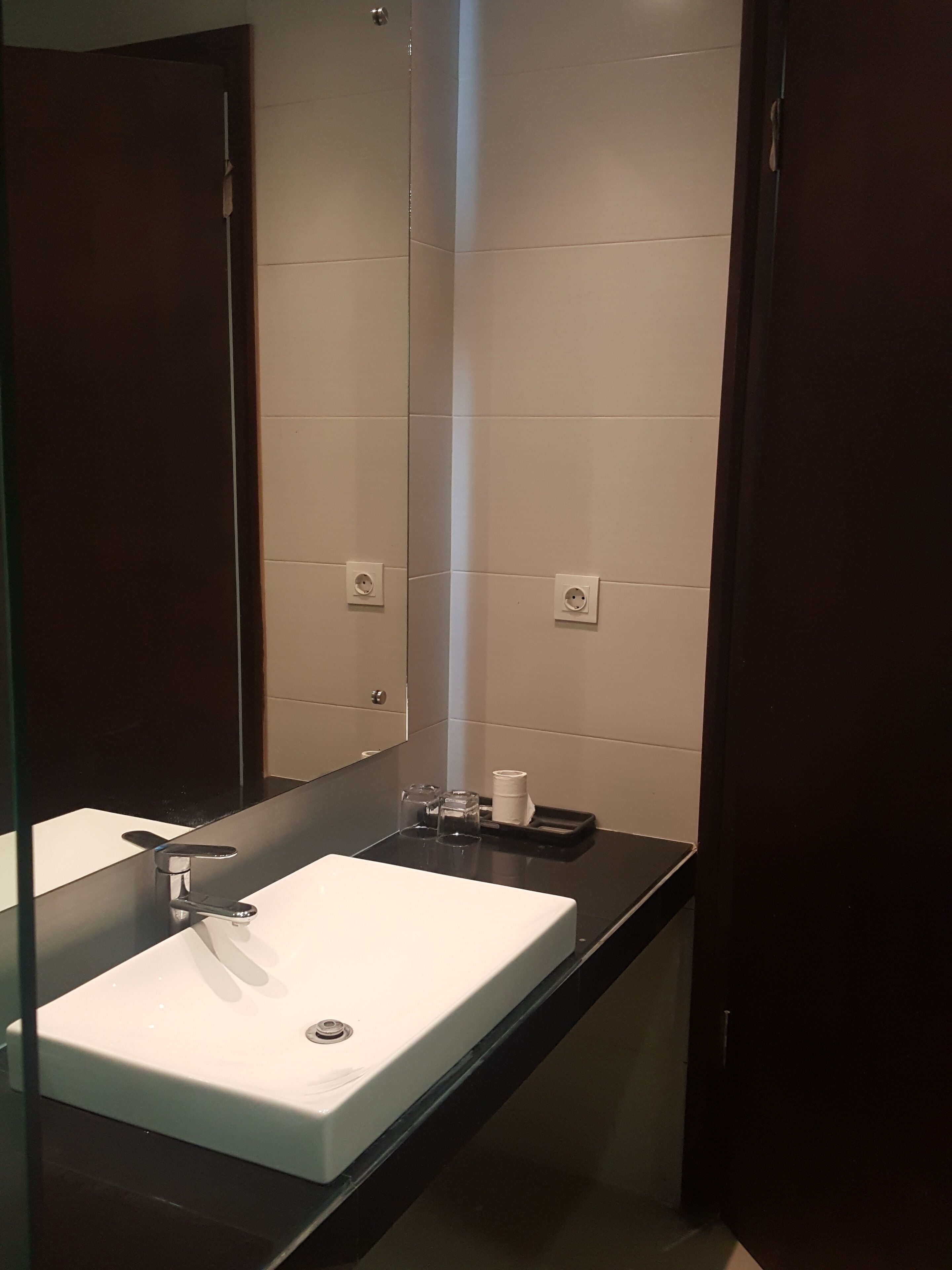 Un baño moderno con un lavamanos blanco, un espejo y una encimera negra.