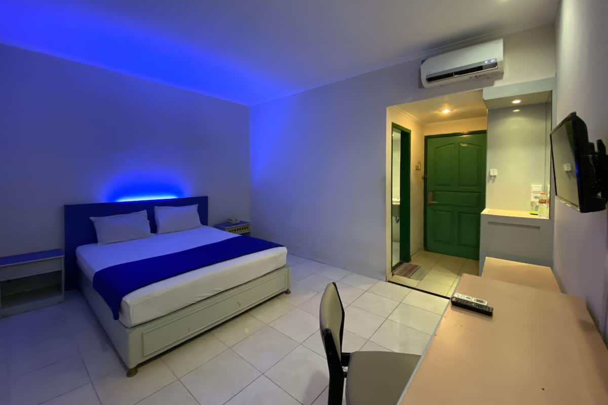 A hotel room with a bed, a desk, a chair, an air conditioning unit, and a green door.