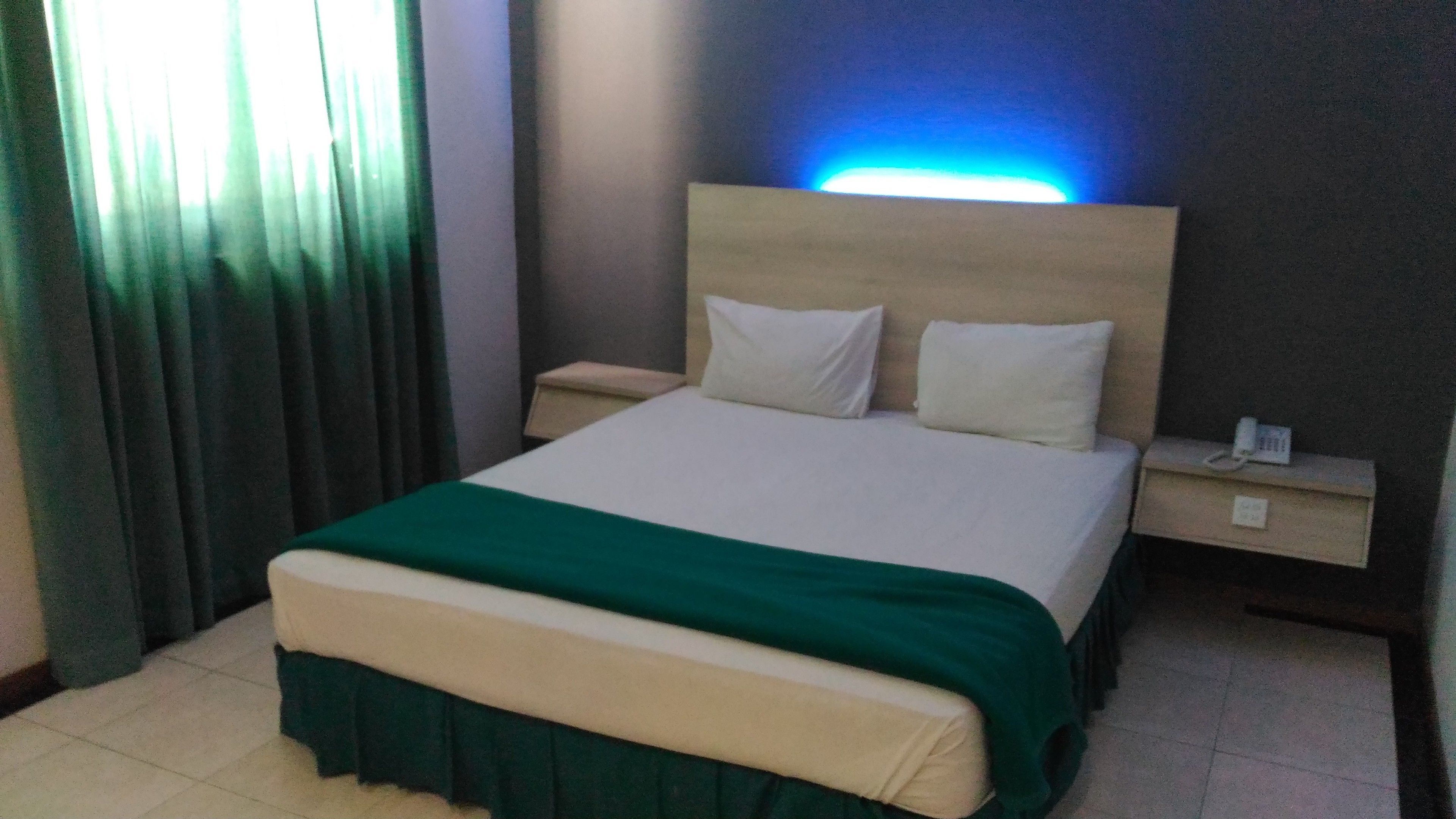 Una habitación de hotel con una cama, una mesita de noche, un teléfono y una lámpara.