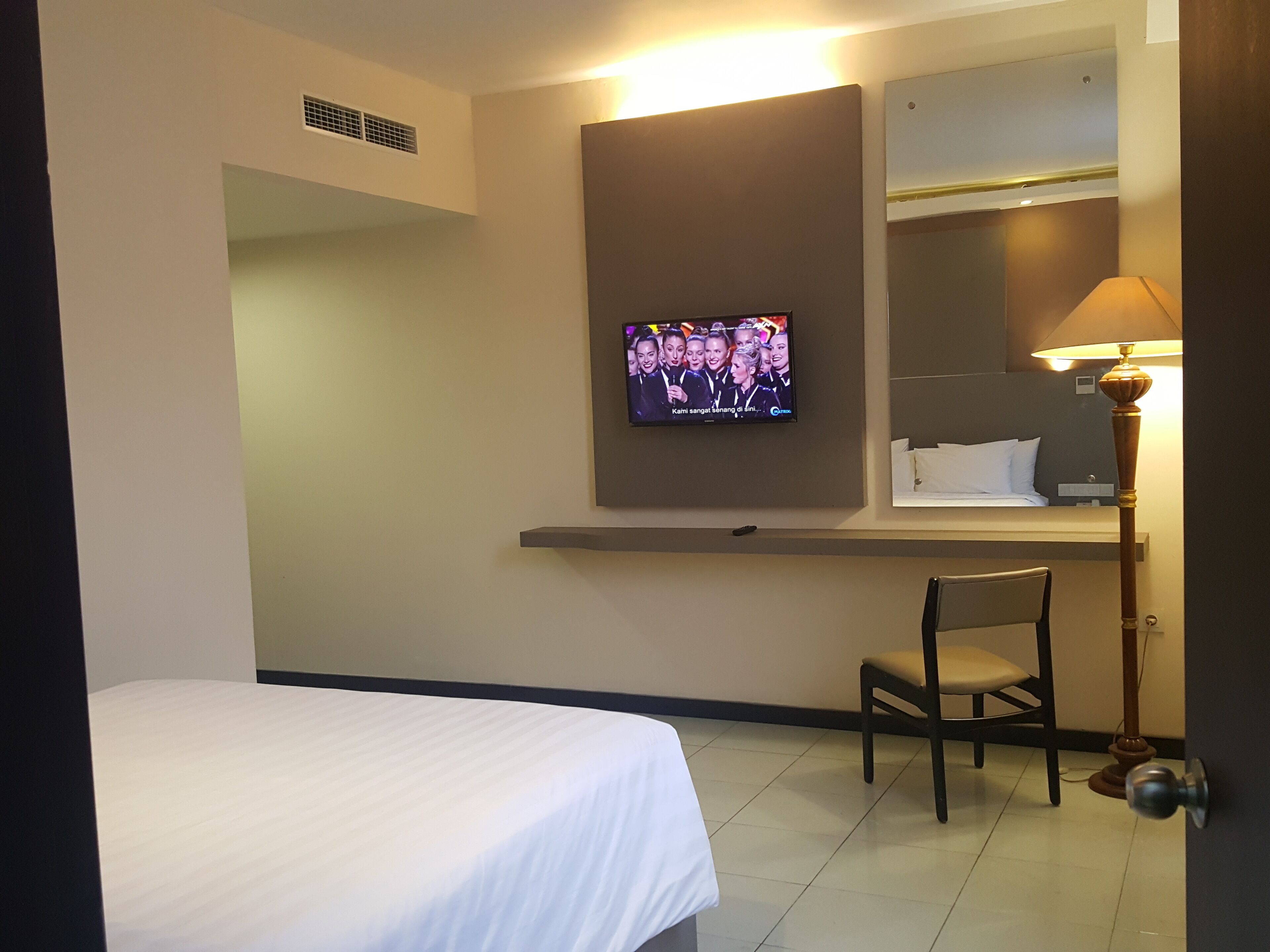 Une chambre d’hôtel comprenant un lit, une chaise, un téléviseur fixé au mur, une lampe et un miroir.