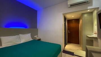 Una habitación de hotel con cama, mesita de noche, aire acondicionado y puerta al baño.