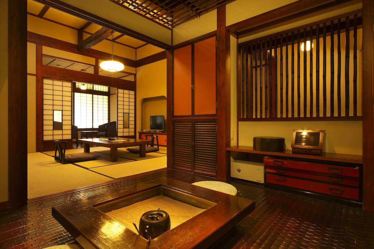 Una habitación japonesa tradicional con suelo de tatami, una mesa baja con un calentador de agua, un televisor y una puerta corredera.