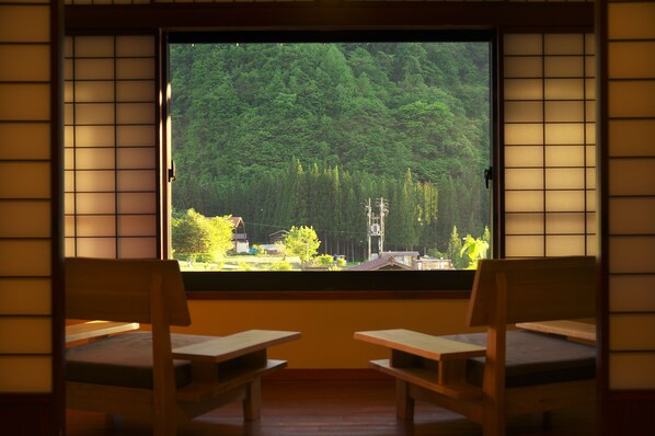 A room with tatami mat flooring, a large window with a view of a forest, and two wooden benches. - Yamaboushi (Takayama)