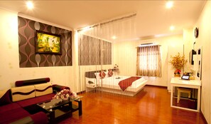 A hotel room with a bed, a sofa, a coffee table with flowers, a TV, and a bathroom with a mirror and a sink. - Linh Phuong 2 Hotel (Can Tho)