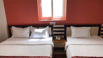 A hotel room with two beds, a window, and a bedside table with a phone.