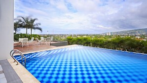 Una piscina sul tetto con vista panoramica sulla città, circondata da palme e poltrone relax.