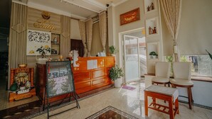 A hotel lobby with a reception desk, a seating area with two chairs, a decorative plant, and a wall with framed pictures. - Tulip Hotel Can Tho (Can Tho)