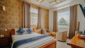 A hotel room with a large bed, two chairs, a desk, and a view of the outdoors. - Tulip Hotel Can Tho (Can Tho)