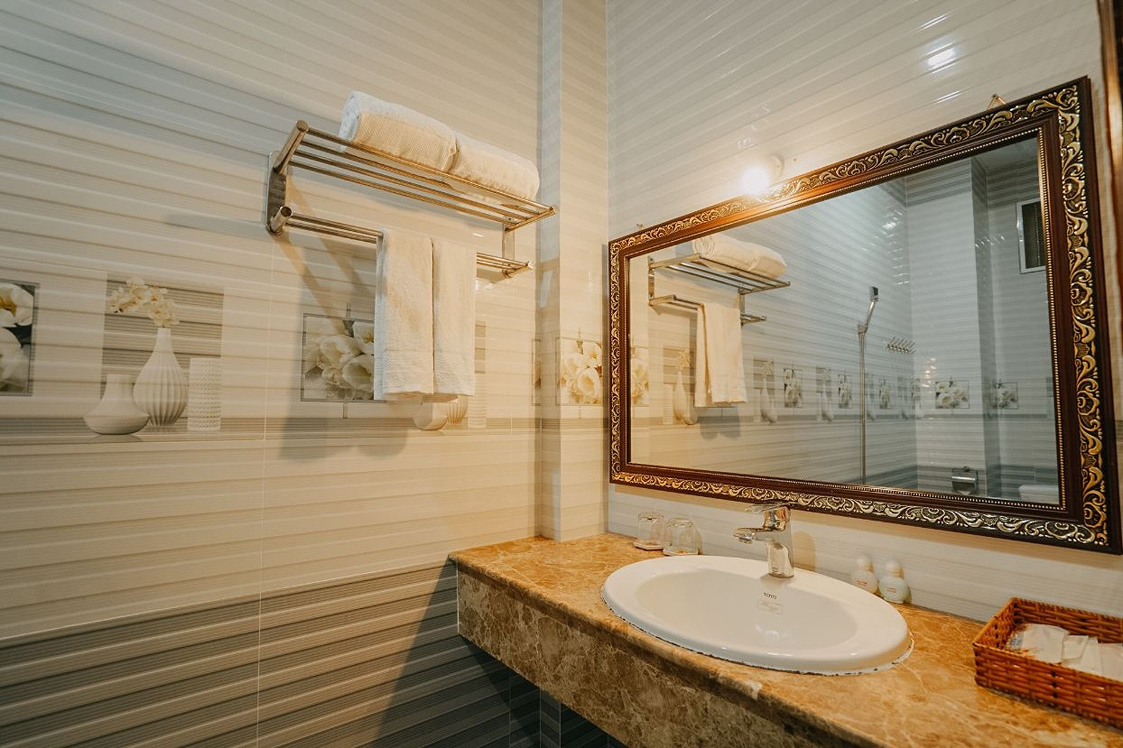 Un baño con lavamanos de mármol, un espejo grande y decorativo, y barras para toallas en la pared.