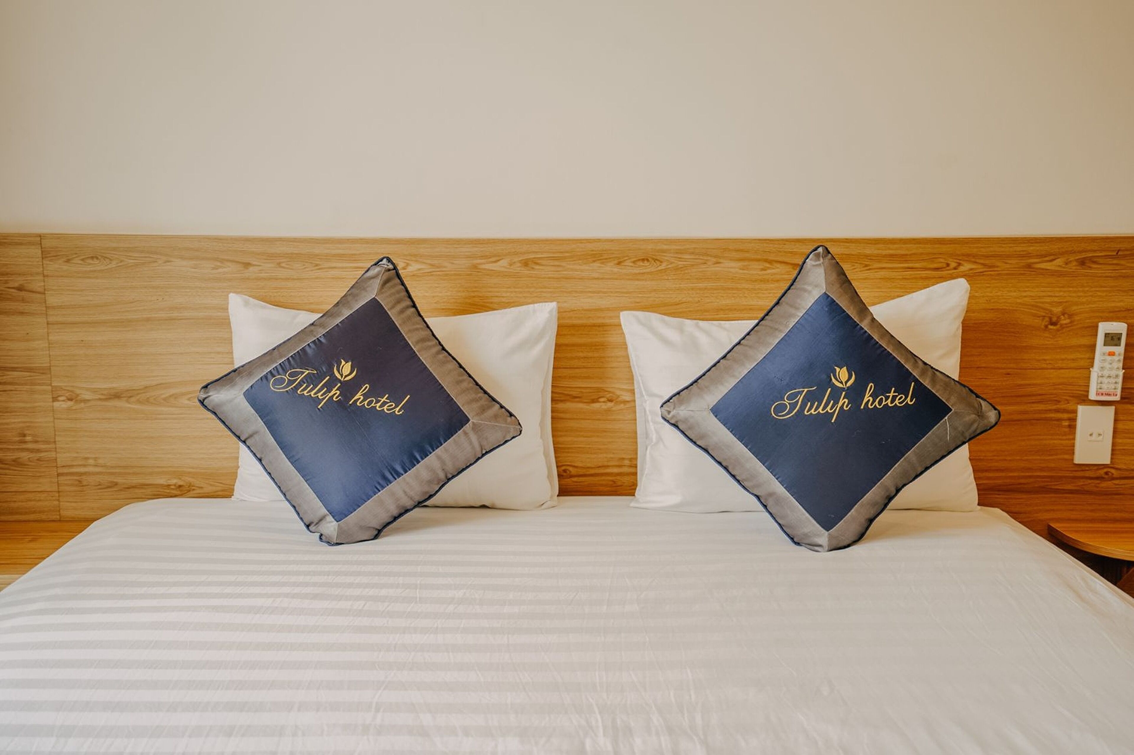 Ett hotellrum med en sänggavel i trä, två kuddar med broderad texten ”Tulip hotel” och ett vitt överkast.