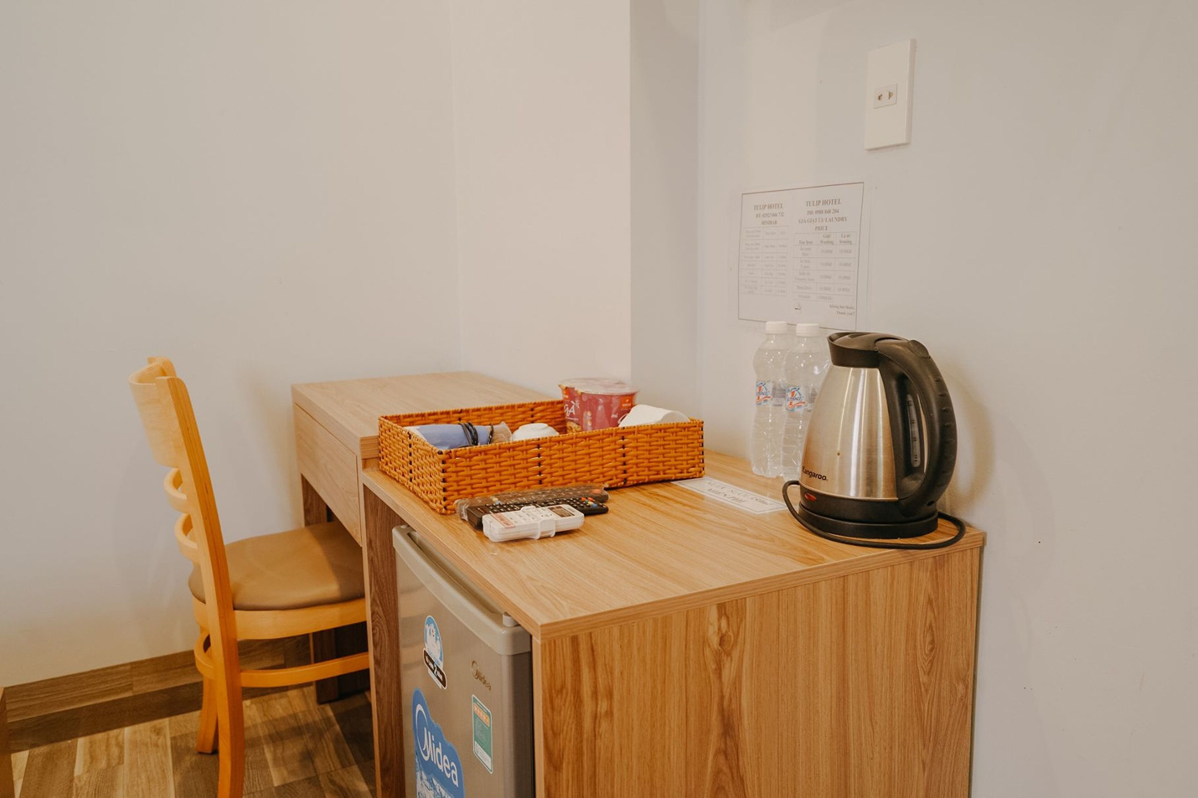 Una pequeña cocina americana con una mesa de madera, una silla, cafetera, cesta y refrigerador.