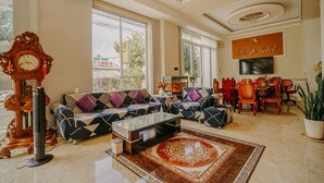 A hotel lobby with a sofa set, a coffee table, a chandelier, and a TV mounted on the wall. - Tulip Hotel Can Tho (Can Tho)