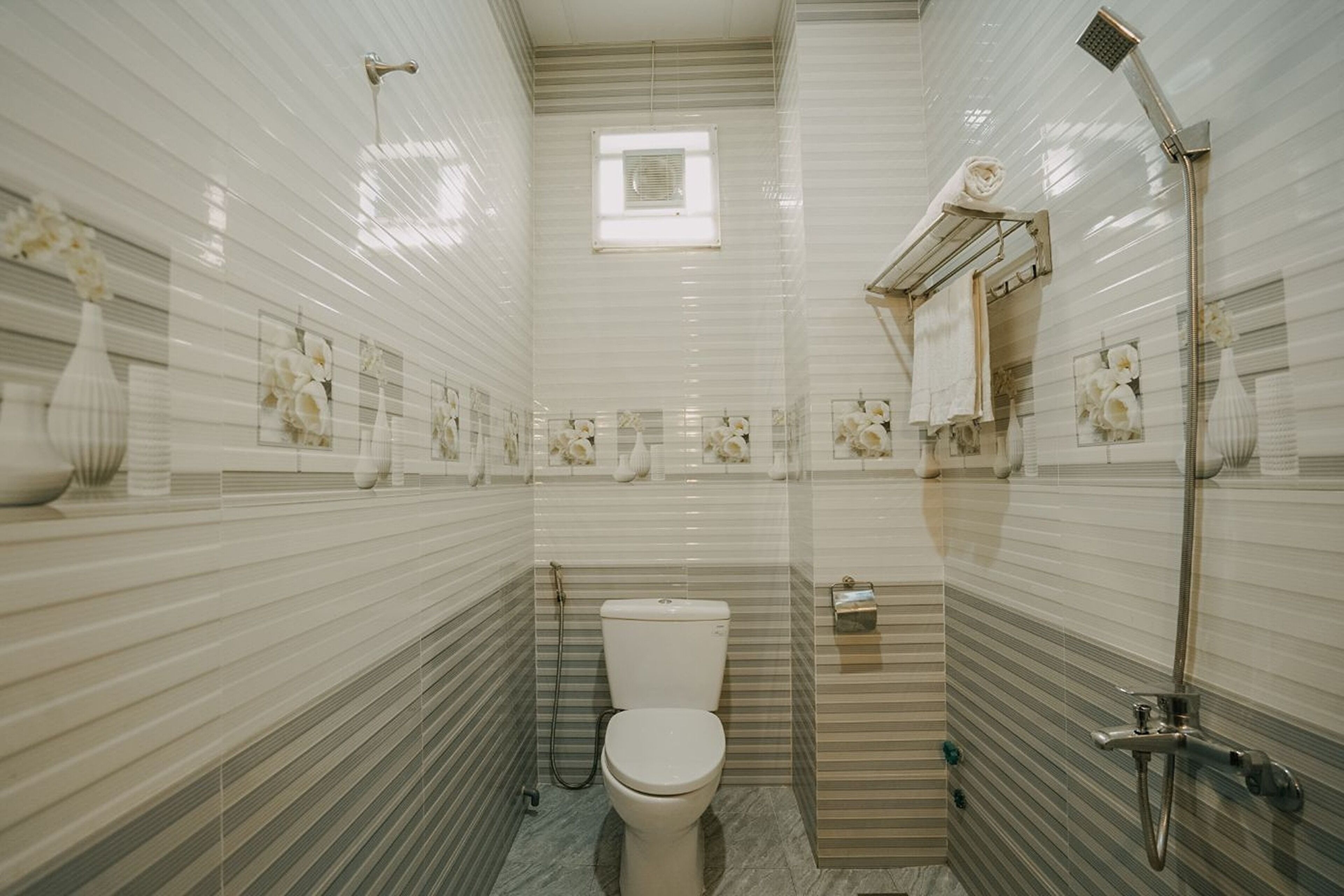 Et badeværelse med toilet, bruser og et vindue.