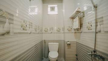 Et badeværelse med toilet, bruser og et vindue.