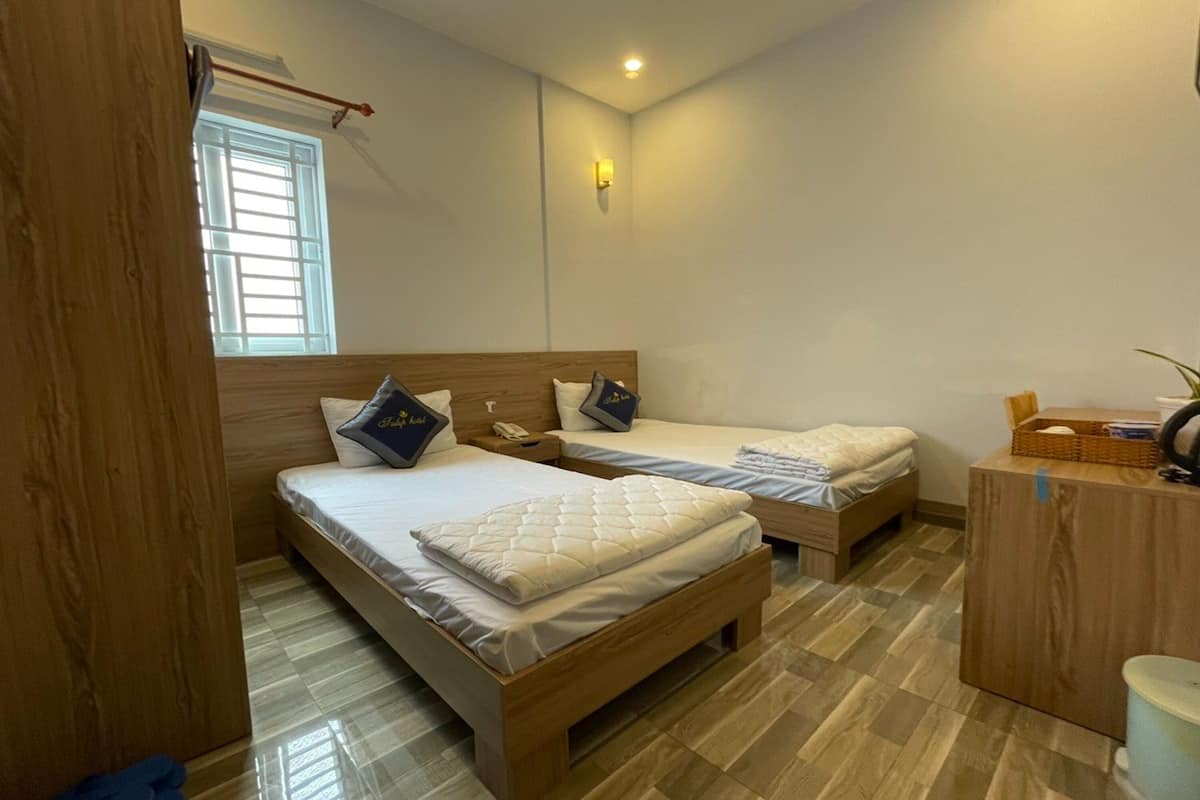 A bedroom with two wooden beds, a small desk, and a window with blinds.