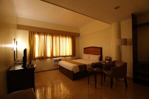 Une chambre d’hôtel avec un lit, un bureau, une chaise, une lampe et une fenêtre avec des rideaux.