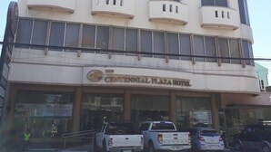 Een meerlaags hotel met een platte gevel, balkons en een bord met de tekst Centennial Plaza Hotel op de begane grond.