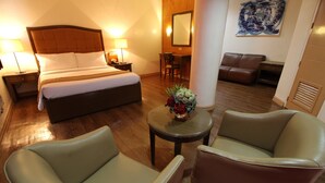Een hotelkamer met een bed, twee stoelen, een kleine tafel met bloemen, een bureau en een bank.