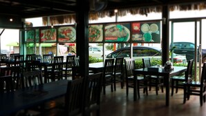 Un comedor interior con mesas y sillas, ventanas amplias y vista a coches estacionados afuera.