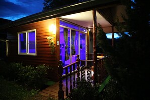 Una cabaña de madera con un porche, una pequeña terraza y un ventanal con cortinas.