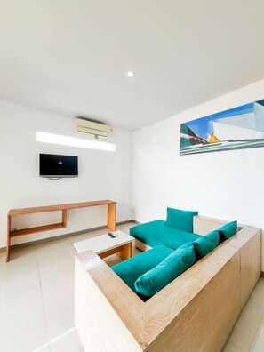 A modern living room with a wooden sofa, a flat-screen TV, and a painting on the wall. - Apple Suite Apartment (Keroboken Kelod)