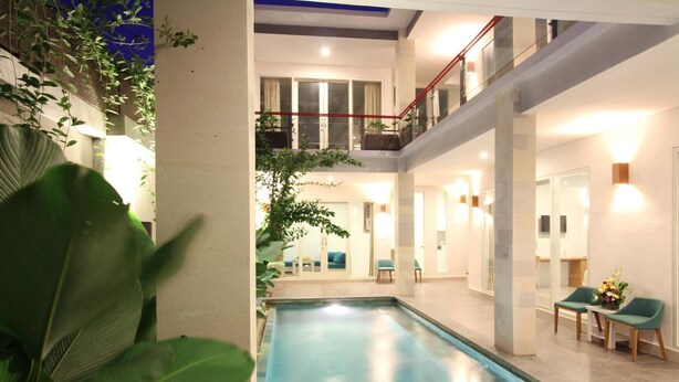 A modern indoor pool area with a glass balustrade, a staircase, and a seating area with chairs and a table. - Apple Suite Apartment (Keroboken Kelod)