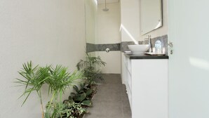 A narrow hallway with a bathroom on the right, featuring a sink, mirror, and shower. - Apple Suite Apartment (Keroboken Kelod)
